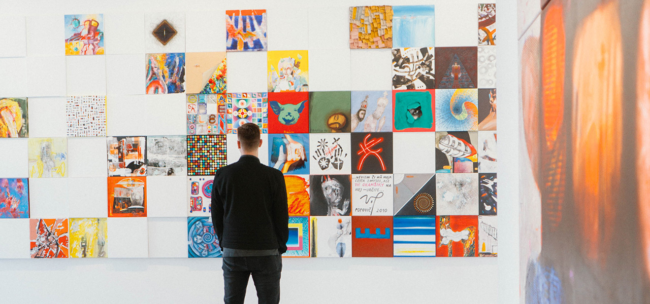 A man casually standing in front of a wall of art