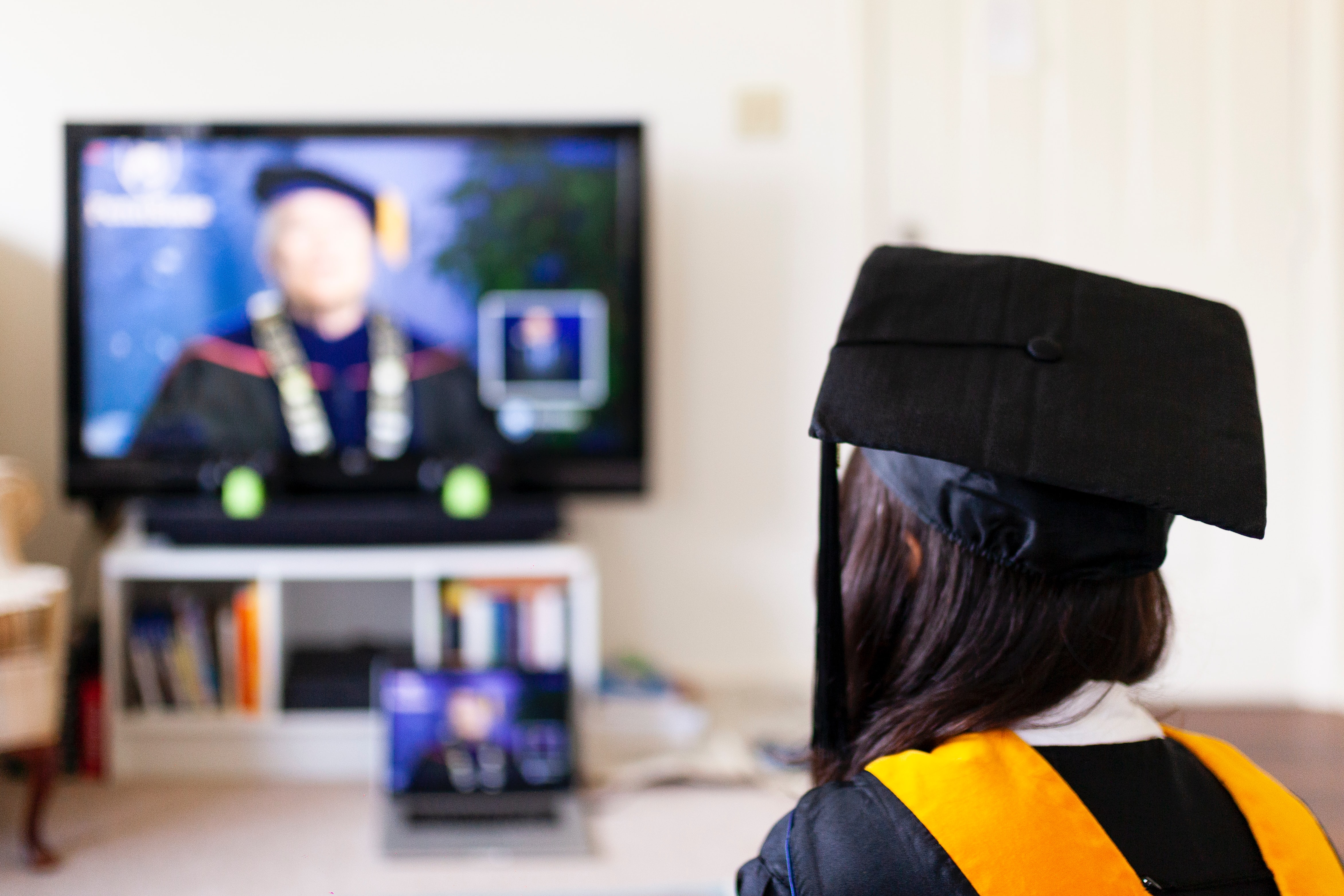 student in cap and gown attending a virtual college graduation ceremony