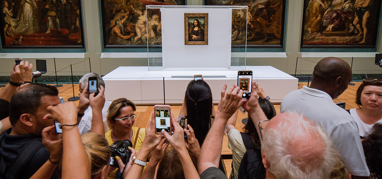 Photo of a group of people taking pictures of the Mona Lisa on their phones