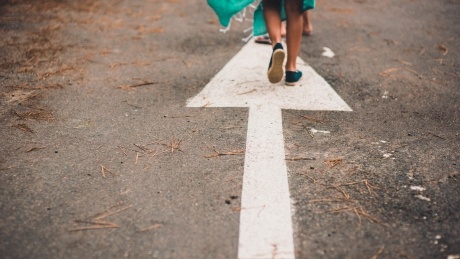 A low shot of a person's feet on a white arrow on a road