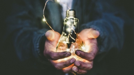 person holding a bright lightbulb against a dark background 