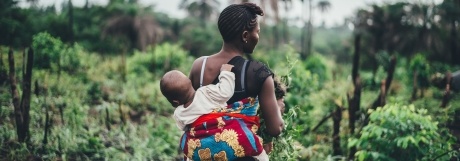 Woman in tropical setting with baby strapped to her back